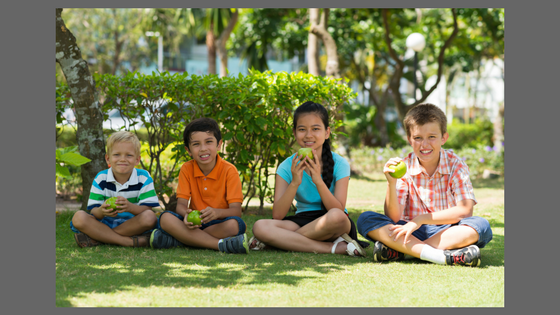 kids sitting on a lawn eating apples